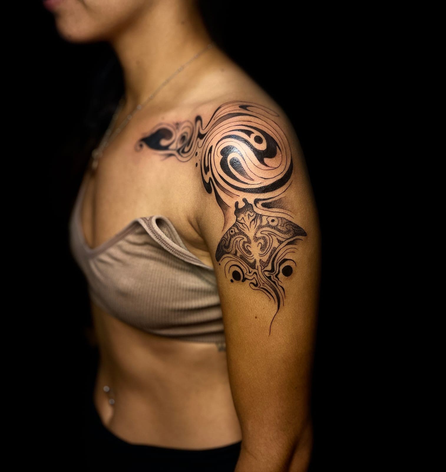 Tatuaje tribal contemporáneo en blackwork sobre el hombro y el brazo, con curvas envolventes y degradado suave hacia la piel